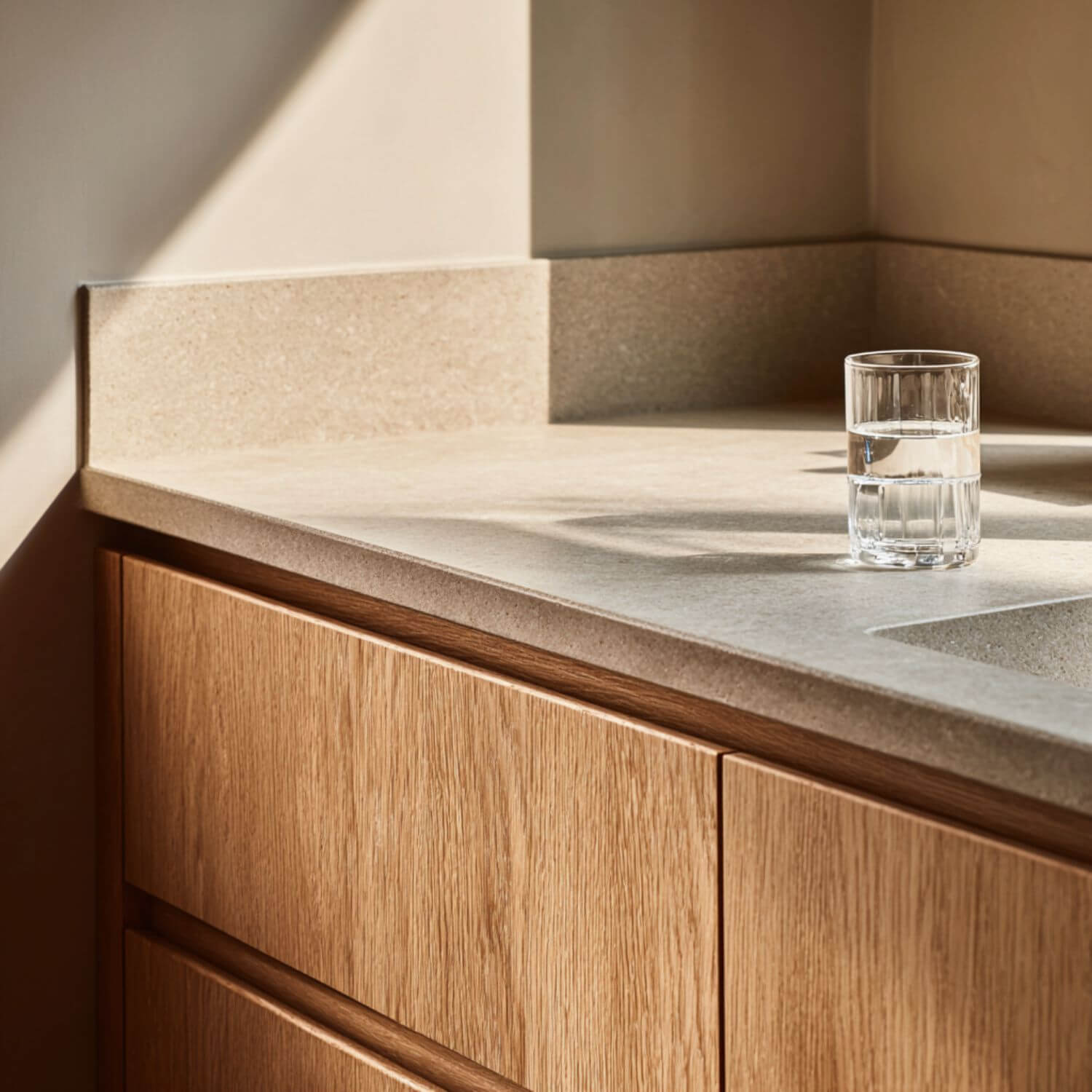 Cocinas que cansan: detalle editorial realista de encimera y mueble en madera clara con piedra mate, luz cálida y diseño sobrio y funcional.