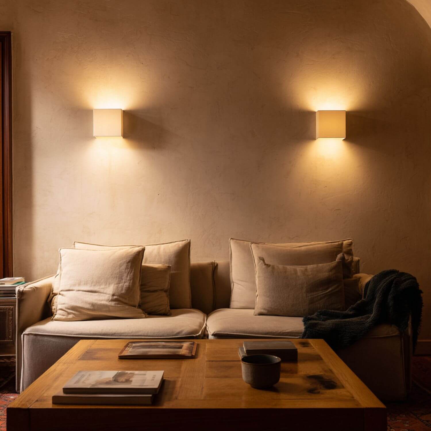 Salón minimalista con sofá claro e iluminación cálida de apliques en pared de estuco, ejemplo de atmósfera acogedora y equilibrada.