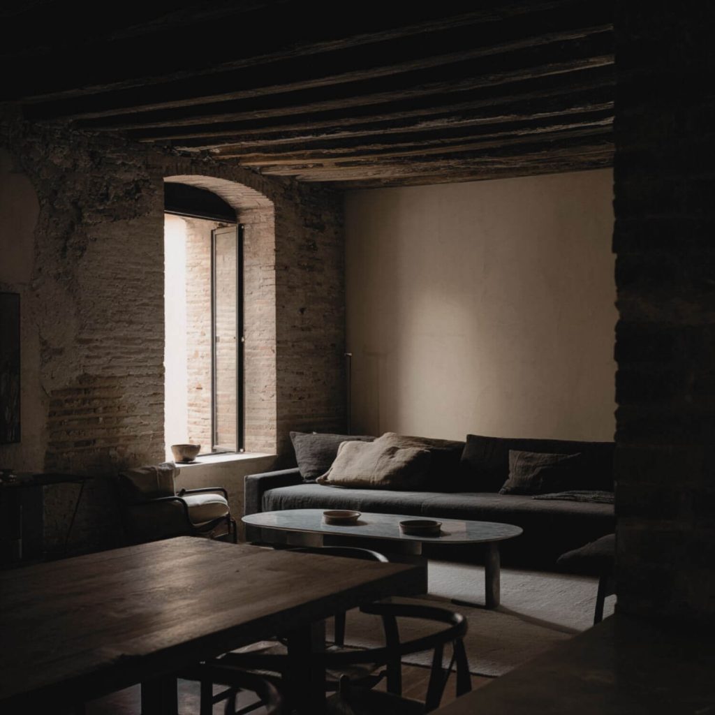 Salón en vivienda de Sevilla con muros originales, luz natural lateral y atmósfera sobria y litúrgica diseñada por Fran Linares. Interiorismo Sevilla.