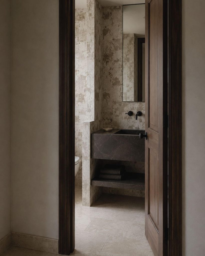 Proyecto Recodo: baño de vivienda tradicional andaluza reinterpretada con lavabo de piedra oscura, revestimiento pétreo y carpintería de madera en un proyecto de interiorismo en Sevilla.
