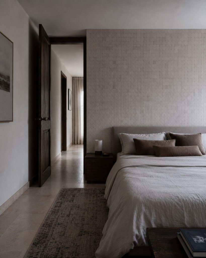 Dormitorio sereno con madera oscura, textiles neutros y paso hacia el vestidor en proyecto de interiorismo en Sevilla.