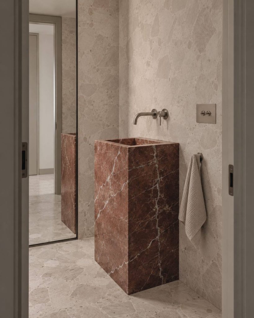 aseo con lavabo monolítico de mármol rojo alicante y revestimiento de piedra clara